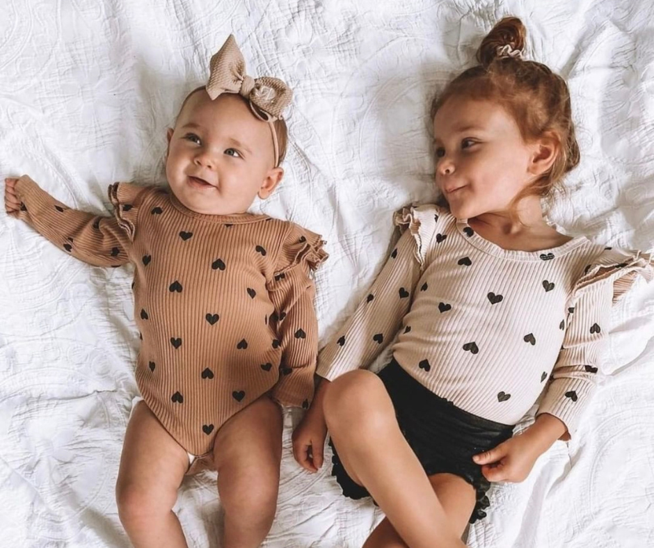 Two little girls dressed in little eedie heart print rompers with flutter sleeves